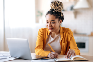 Lachende pabo-studente die geconcentreerd aan het studeren is met een laptop en een studieboek voor de LKT-rekentoets.